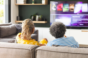Senior African American woman and senior biracial woman are sitting on a couch, watching TV at home