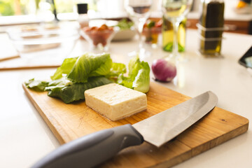 A block of cheese and a knife rest on a wooden cutting board