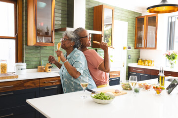 Senior African American woman and senior biracial woman enjoy a dance in a sunny kitchen