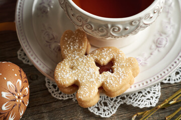 Bunny shaped homemade Linzer cookie with a cup of tea and an Easter egg decorated with wax