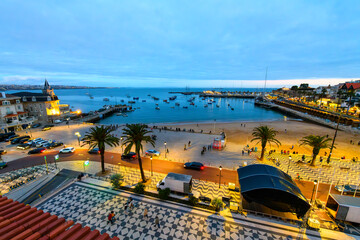 Evening view of the Praia da Ribeira beach, historic fort, marina, sea, boardwalk and illuminated...