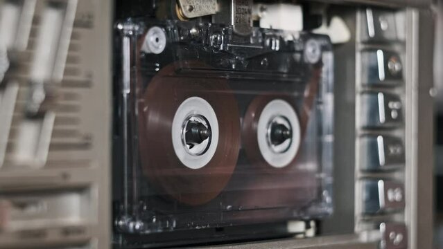 Audio tape recorder playback. Insert and eject vintage transparent audio cassette close-up. Record player playing an old tape. Retro tape reels rotate in a deck. Rec conversations, calls, archive, 80s
