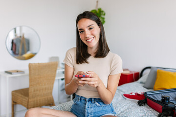 Portrait of pretty woman using mobile phone sitting on bed at home. Beautiful female chatting on...