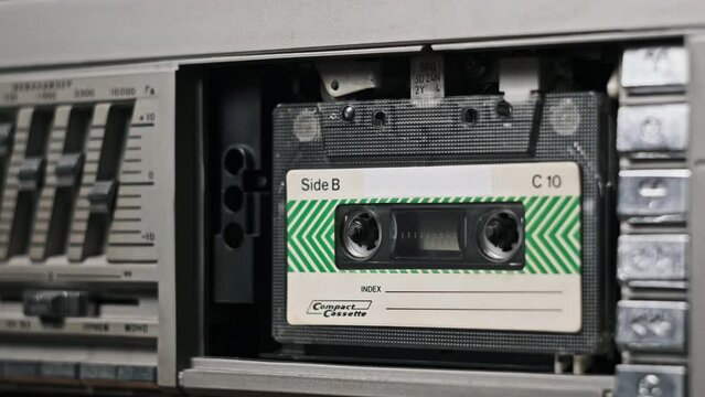 Insert an audio cassette in a tape recorder and playback, eject, close-up. Playing old audio. Vintage record sound in retro player. Tape reels rotate in a deck. Rec conversations, calls, archive, 80s