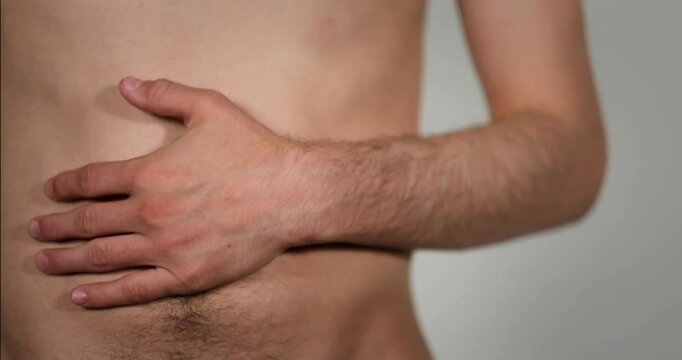 A man moves his hand across his belly button. He has bare skin, an olive complexion, and a little bit of body hair. 