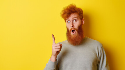 Homem ruivo barbudo com um dedo levantado e expressão de impressionado isolado no fundo amarelo
 