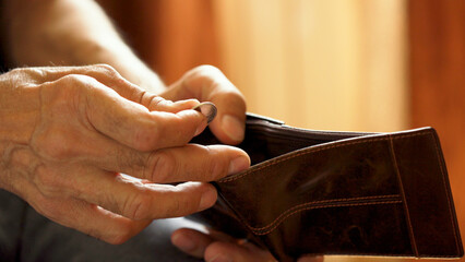 An elderly man's hands, covered with knotted veins, search for coins in his wallet