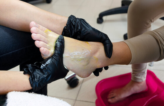 Exfoliación e hidratación de pies para pedicura profesional con gel extracto de maracuyá. Manos de pedicurista o esteticista con guantes de látex exfoliando pie de mujer joven en spa.  
