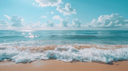 Crystal clear waves crashing on a sandy beach under a sunny sky with fluffy clouds.