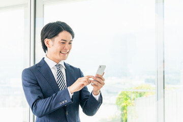 オフィスでスマホを使うアジア人男性ビジネスマン
