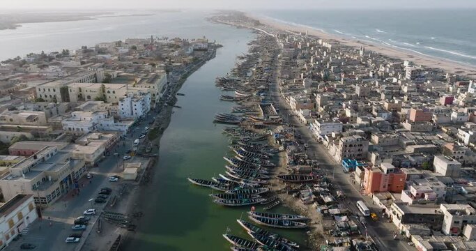 Aerial fly over.   Colourful pirogue boats lie anchored in the polluted Senegal River. Plastic pollution, Saint-Louis, Senegal, Unesco World Heritage Site