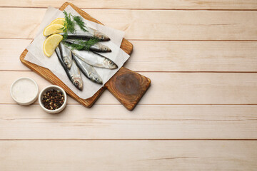 Fresh raw sprats, lemon and dill on light wooden table, top view. Space for text