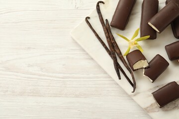 Glazed curd cheese bars, vanilla pods and flower on white wooden table, top view. Space for text