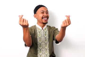 Smiling Indonesian Muslim man in koko shirt and peci makes a mini heart gesture with his fingers,...