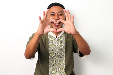 Smiling Indonesian Muslim man in koko shirt and peci makes a heart gesture with his hands,...
