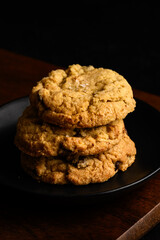 Sweet treat, dark and moody image of three homemade fancy chocolate chip cookies stacked on a dark wood board
