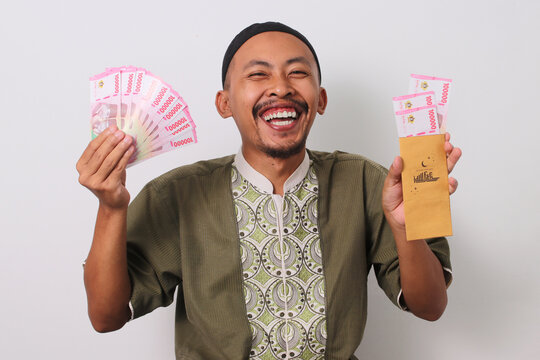 Indonesian Muslim man holds a brown envelope filled with Indonesian Rupiah banknotes, representing Angpao Lebaran or Eid Money Gift given during Eid al-Fitr. Isolated on a white background