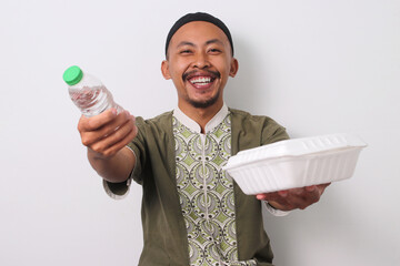An Indonesian Muslim man in koko and peci holds a tray with mineral water and takjil, ready to...