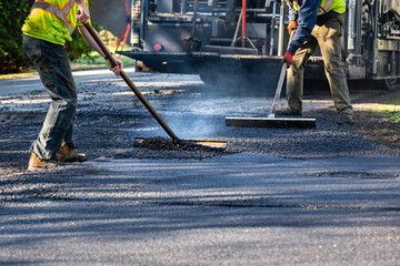 Residential street repaving project, workers in safety clothes smoothing fresh hot asphalt behind...