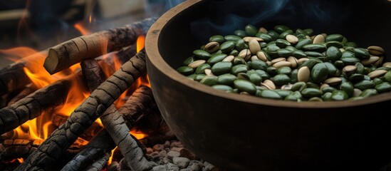 A metal bowl filled with green beans is placed on top of a fire, with charcoal burning underneath. The green beans are being cooked and heated up by the flames and smoke. - Powered by Adobe