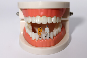 Two miniature old men sitting on a model of their teeth. The burden of dental expenses for the elderly.
