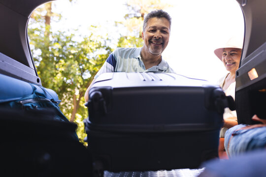 Senior biracial couple loads luggage into a car, ready for a trip