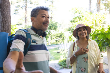 Senior biracial couple enjoys a sunny day outdoors, with the man extending his arm as if taking a se