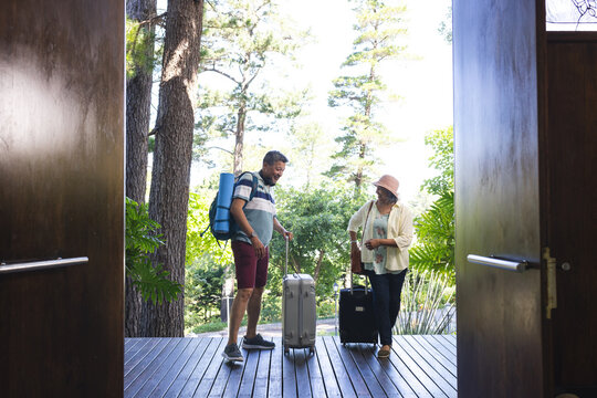 Senior biracial couple with luggage entering a wooden-floored vacation home