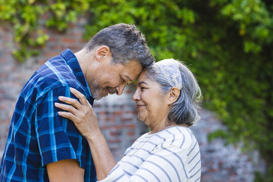 Senior biracial couple shares a tender moment, foreheads touching with affectionate smiles