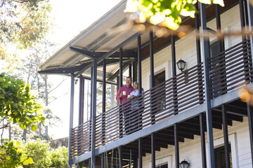 Senior biracial woman and biracial man stand on a porch, enjoying a sunny day