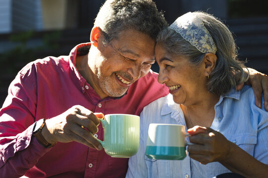 Senior biracial couple shares a joyful moment with a toast of coffee mugs