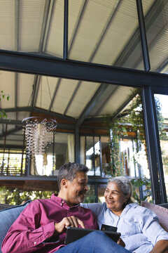 Senior biracial couple enjoys a moment together on a couch, surrounded by plants, with copy space