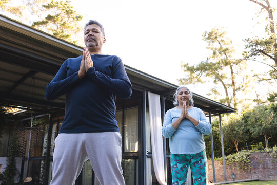 Senior biracial couple practices yoga outdoors, at home