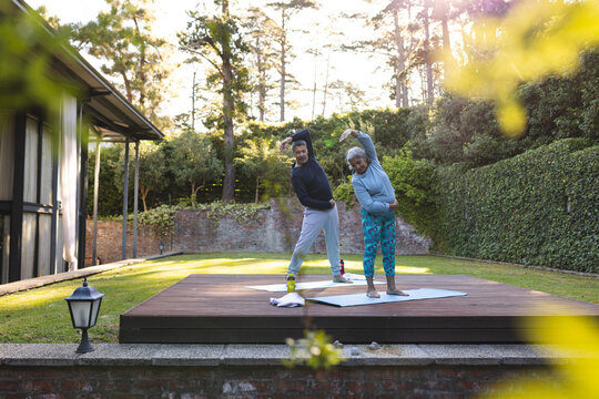 Senior biracial woman and man are stretching on a yoga mat outdoors at home