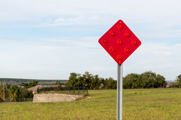 A red traffic sign on a metal pole. There's a grassy meadow and trees in the background. The...