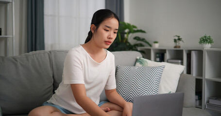 Selective focus, Young attractive woman is using laptop to watch online yoga lessons sitting on sofa with eyes closed do meditation in the living room at home