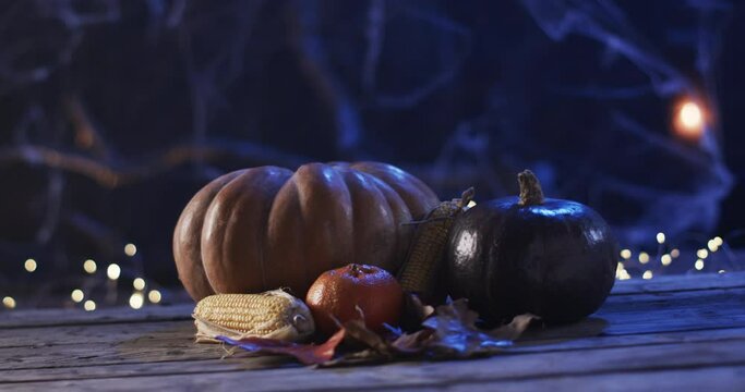 Pumpkins and corn rest on a wooden surface at night, with copy space