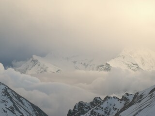 Majestic peaks obscured by billowing clouds, their tops adorned with a pristine layer of glistening snow.