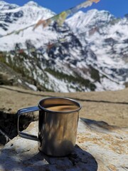 A steamy cup of coffee perches atop a weathered rock, with snowy hill in background