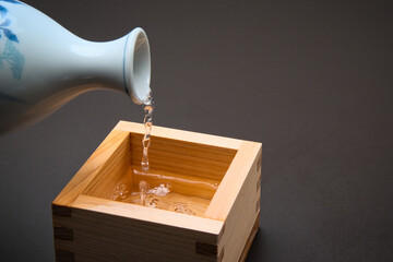 Pouring sake into a square wooden container called a "Masu".