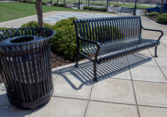 Black metal park bench and trash can in public park.