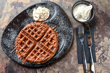Nutella Waffle with chocolate, whipped cream, knife and fork served in dish isolated on dark...