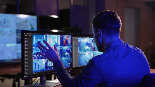 Security system operator looking at CCTV footage at desk in control room