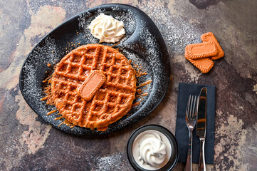 Lotus Waffle with chocolate, whipped cream, knife and fork served in dish isolated on dark background top view cafe dessert food