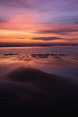 sunset sky is reflecting in the low tide draining waters of a beach in Sylt Island, Germany