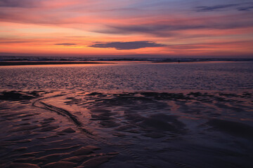 Fototapeta na wymiar sunset sky is reflecting in the low tide draining waters of a beach in Sylt Island, Germany