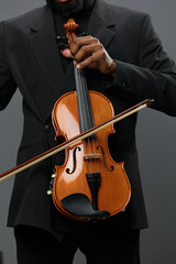 African American man in a suit playing a violin in front of a black background, creating a soulful melody