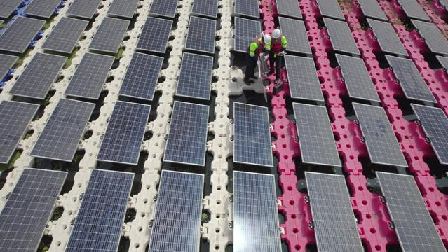 Aerial view and circulate two technician workers use tablet to discuss about maintenance solar cell panels over water reservoir.
