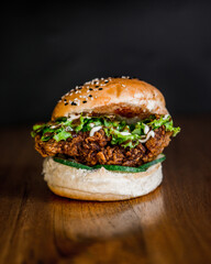 Top-down view of a chicken sandwich on a toasted bun with sesame seeds, vegan, and meat on a wooden table