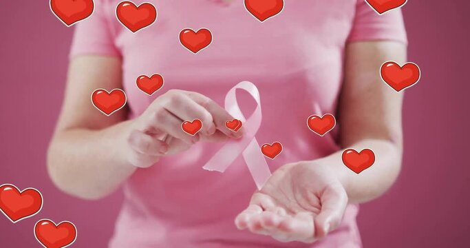 Animation of hearts over caucasian woman holding pink ribbon